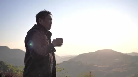 Asian man in a winter jacket enjoys a hot drink while admiring Stock Footage 324906505