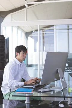 Asian man working on desktop computer in modern office, focusing on task, c.. Stock Photos