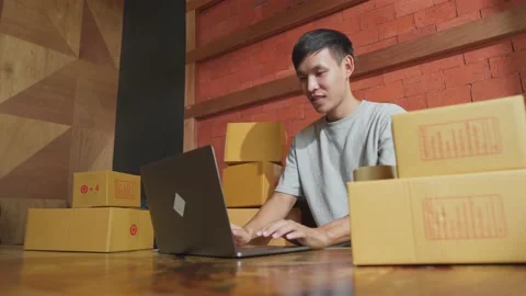 Asian man working laptop computer from home floor with postal parcel. Stock Footage 211562001