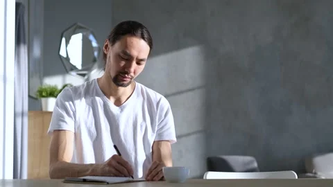 Asian man writes in a notebook while sitting at home Stock Footage 151878220