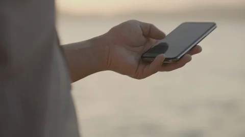 Asian man's hand are using a smartphone at the seaside at sunset. Stock Footage 100934756