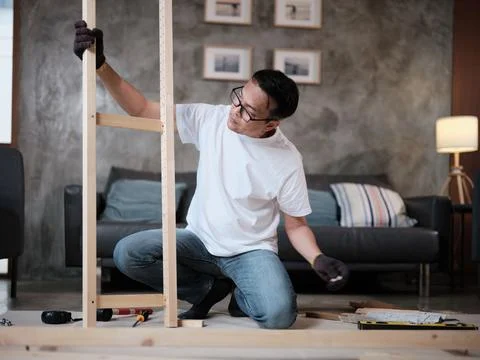 Asian mature man self-assembles wooden furniture with strength and accuracy. Stock Photos