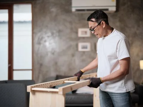 Asian mature man self-assembles wooden furniture with strength and accuracy. Stock Photos