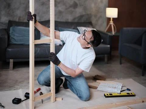 Asian mature man self-assembles wooden furniture with strength and accuracy. Stock Photos