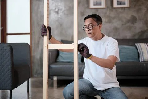 Asian mature man self-assembles wooden furniture with strength and accuracy. Stock Photos