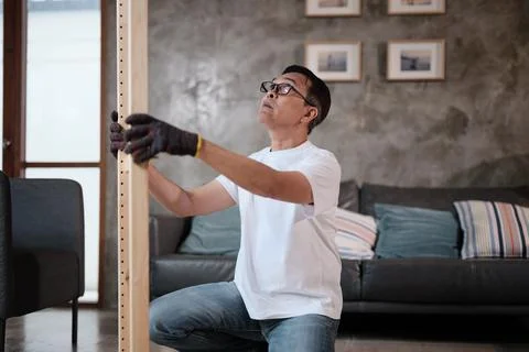 Asian mature man self-assembles wooden furniture with strength and accuracy. Stock Photos