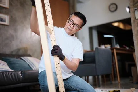 Asian mature man self-assembles wooden furniture with strength and accuracy. Stock Photos