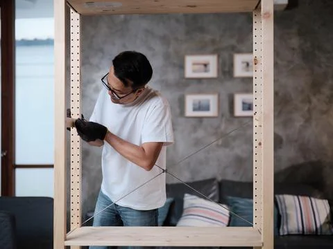 Asian mature man self-assembling flat-pack furniture for home improvement. Stock Photos