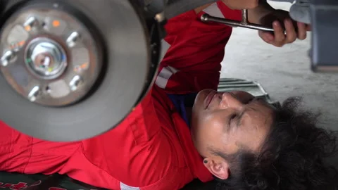 Asian mechanic lying under car using wrench tightening nut repairing undercar Stock Footage 147369841