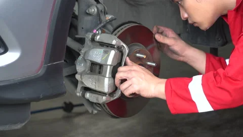 Asian mechanic man in red uniform car brake repairing in workshop at auto car Stock Footage 147369892