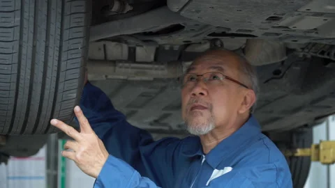 Asian mechanic senior man  checking  brake ,tyre, undercarriage of a car in w Stock Footage 147368752
