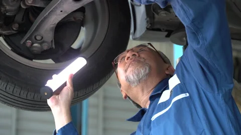 Asian mechanic senior man with flashlight checking brake,tyre, undercarriage Stock Footage 147369045