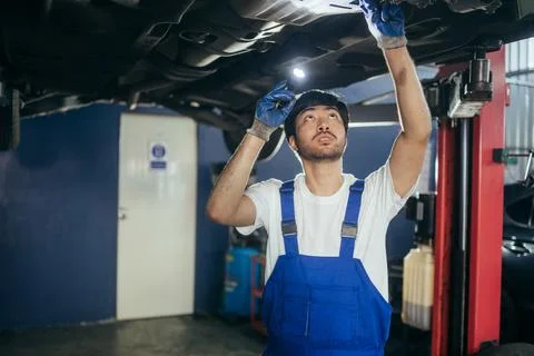 Asian mechanic using flashlight checking under car broken part at auto repa.. Stock Photos