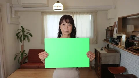 Asian middle aged lady holding green board for chromakey edit. Serious. 25P. Stock Footage 221097196
