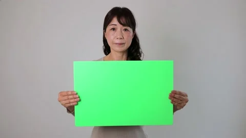 Asian middle aged lady holding green board for chromakey edit. Serious face. Stock Footage 221138445