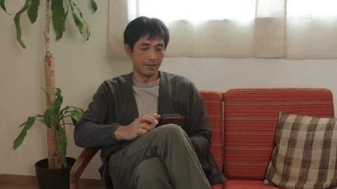 Asian middle aged man checking his smartphone at home. 25P. Stock Footage 224898473