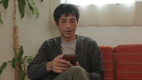 Asian middle aged man checking his smartphone at home. Stock Footage 224902832
