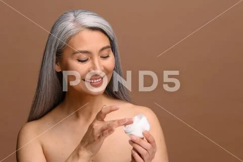 Asian Looking Down Nude - Asian middle-aged woman with naked shoulders, looks down at jar of  anti-aging Stock Photo #201415425