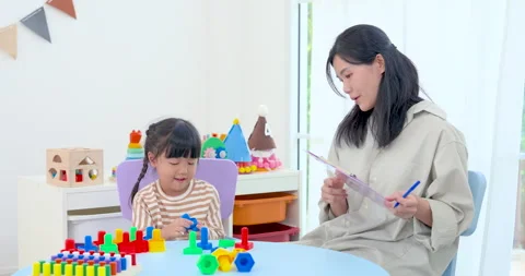 Asian mom checks notes on tablet while preschool daughter concentrates on Stock Footage 332970608