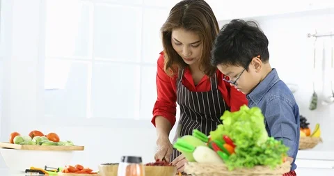 Asian mom teaching her son how to cut vegetable. Stock Footage 99620787