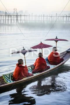 Asian Monks Under Parasols In Canoe On River