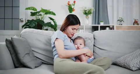 Asian mother hugs her young son and lulls him to sleep on sofa in living room. Stockbeeldmateriaal 313644853
