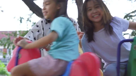 Asian mother pushing her two young daughters on a colorful playground roundabout Stock Footage 335557006