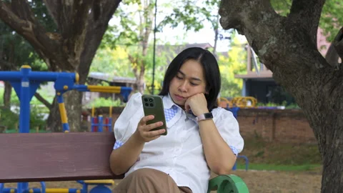 Asian mother using a smartphone while sitting on a bench 動画素材 334093451