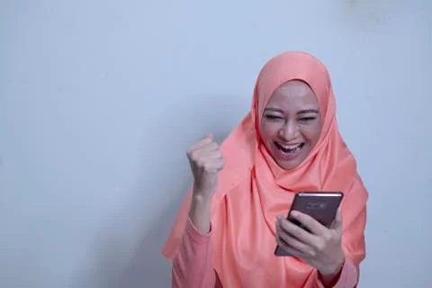 An Asian Muslim lady with happy expression holding smartphone Stock Photos