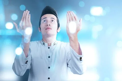 Asian Muslim man standing while raised hands and praying Stock Photos