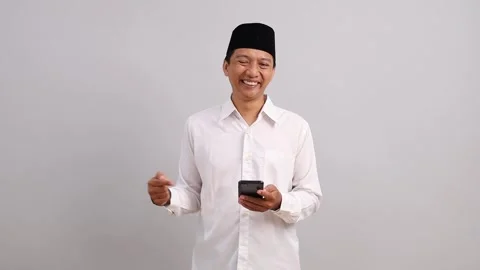 Asian Muslim man using cellphone feeling relieved and happy to get good news Stock Footage 328552172