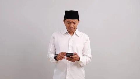Asian Muslim man using cellphone with disappointed and angry expression, in Stock Footage 328552194