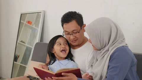 Asian muslim parent, mother, father and child are reading a book at home Stock Footage