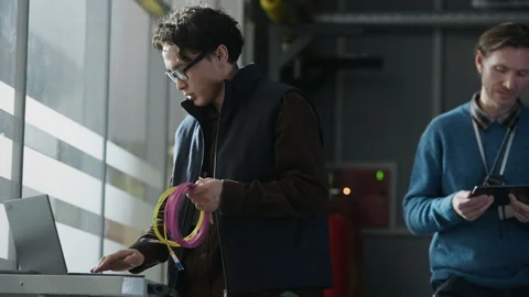 Asian Network Engineer Holding Cable Coil while Working on Laptop in Data Center Stock Footage 330545613