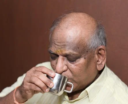 Asian old man drinking coffee or tea from a cup on a brown background Stock Photos