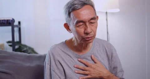 Asian old man having difficulty breathing while sitting on the sofa at home. Stock Footage 245801111