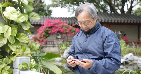 Asian old man use of mobile phone and sitting at chinese garden Stock Footage 83794110