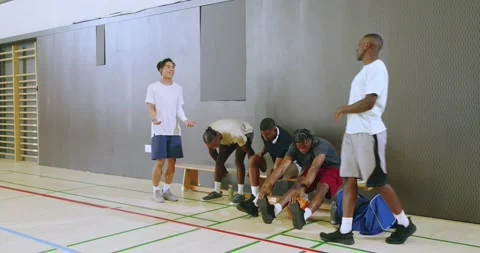Asian player jogging in gym spurring diverse male team lacing shoes passing ball Video stock 341240188