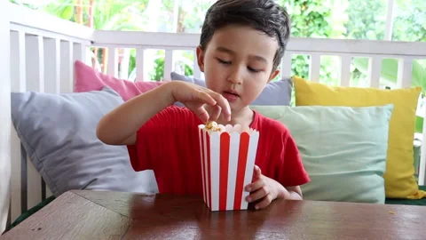 Asian preschooler eats pop corn from red and white box at family cafe. Stock Footage 159521958