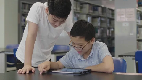 Asian preteens boys using tablet computer at library . Video stock 118381872