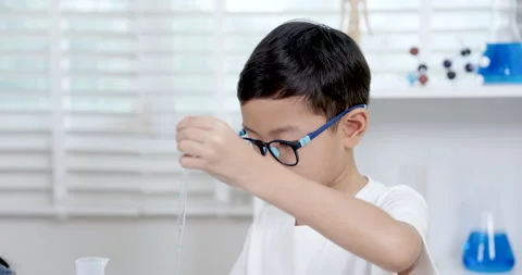 Asian primary school boy performing slowmotion science experiment while holding Stock Footage 311911500