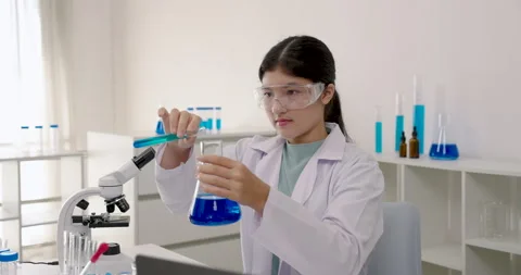Asian primary student in labcoat using glass rod to stir chemical liquid in Stock-Footage 329952935