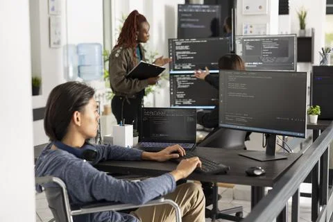 Asian programmer in wheelchair coding at modern office desk Stockfoto's