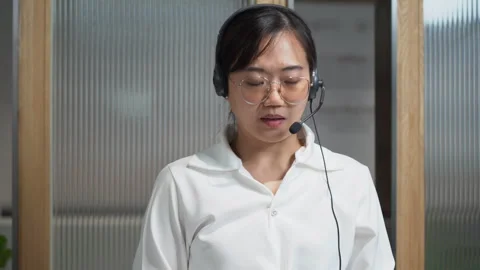 Asian receptionist using headset. Customer service assistant working in off.. Stock Footage 252953274