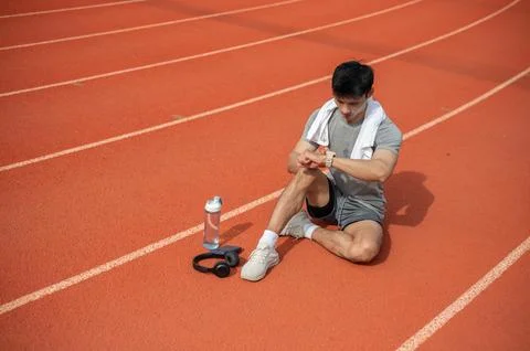 Asian runner man checking smartwatch while sitting on track after training .. Stock Photos
