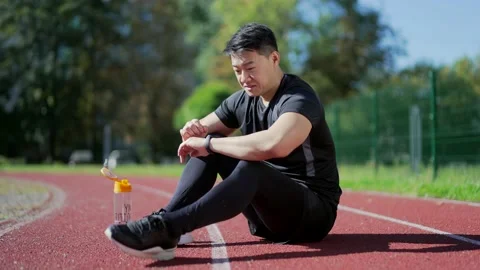 Asian runner resting sitting on treadmill in urban city stadium and checking  Stock Footage 232989377