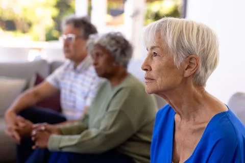 Asian sad senior woman with multiracial friends sitting on sofa in nursing home Stock Photos