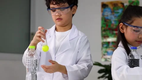 Asian Schoolboy in Lab Coat Holding Test Tube with Yellow Liquid Stock Footage 337927072