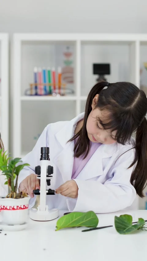 Asian Schoolgirl in Lab Coat Using Microscope for Biology Experiment Stock Footage 342785627