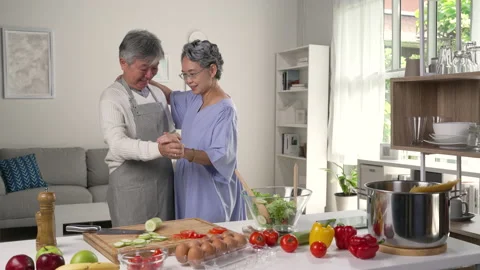 Asian senior couple is dancing while cooking together in kitchen at home. 库存影片 221302490